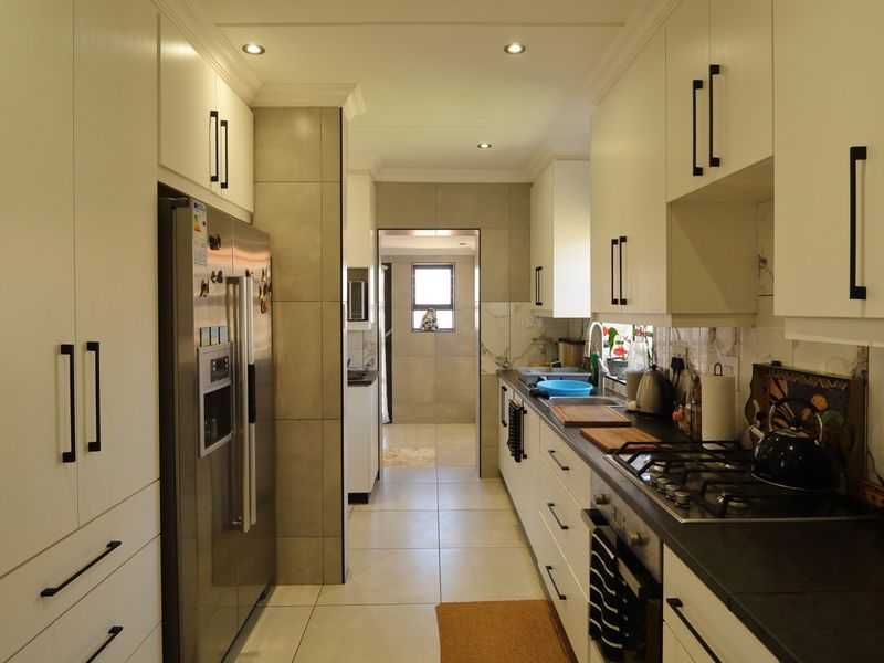 Modern galley-style kitchen featuring sleek white cabinetry, dark stone countertops, a gas hob, and integrated oven, leading into a secondary utility or scullery area.