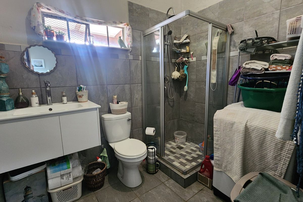 A functional bathroom featuring a glass shower enclosure, wall-mounted vanity with basin, toilet, and grey tiled finishes throughout.