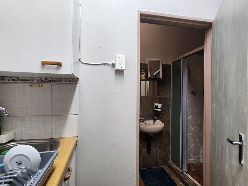 A functional scullery area featuring a sink and cabinetry, with direct access to an adjoining bathroom equipped with a shower and pedestal basin.