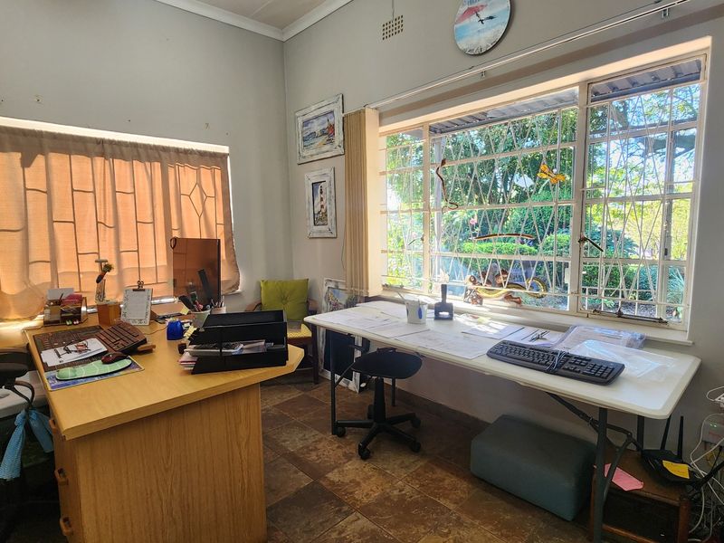 A functional home office space featuring tiled flooring, large windows with security bars, and ample natural light.
