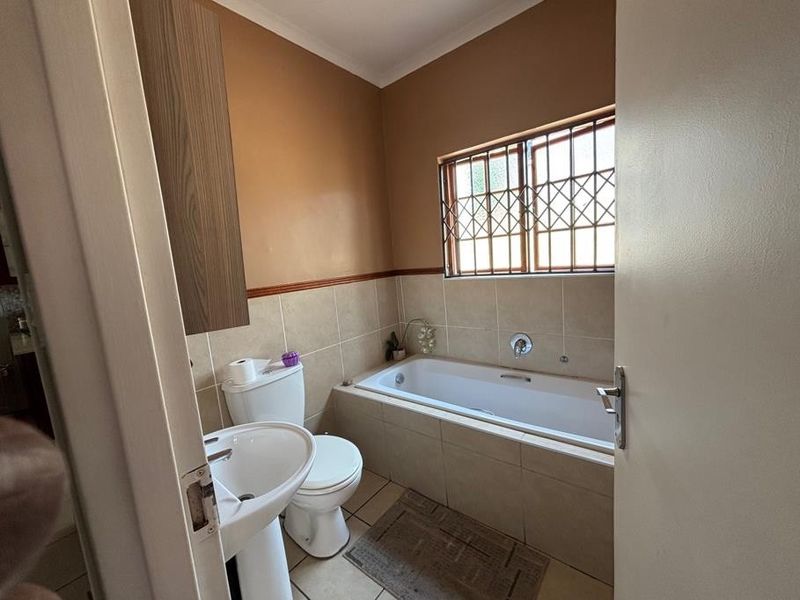 A functional bathroom featuring a built-in bathtub, pedestal sink, toilet, and tiled finishes, complemented by a window with security bars.