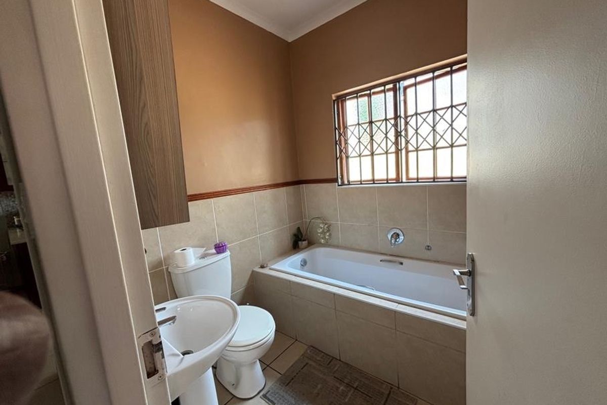 A functional bathroom featuring a built-in bathtub, pedestal sink, toilet, and tiled finishes, complemented by a window with security bars.