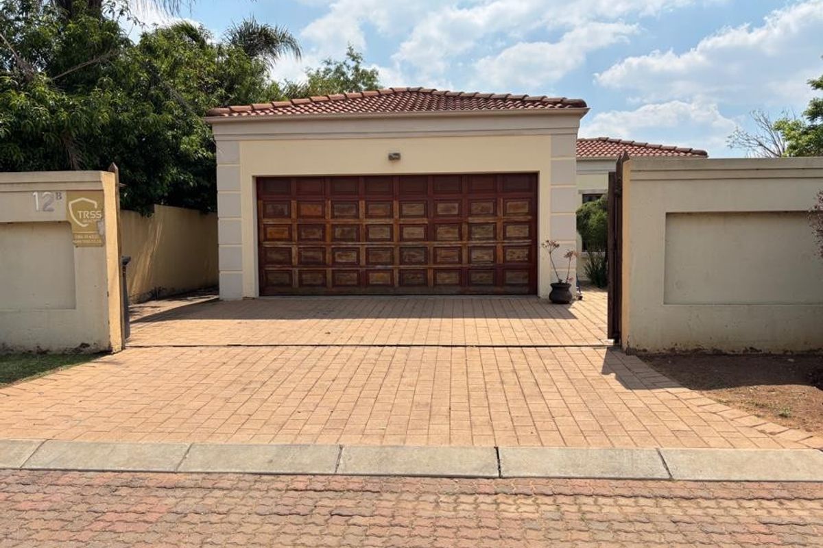 Front elevation of the property featuring a paved driveway, perimeter wall with gated entrance, and a wooden garage door under a tiled roof.