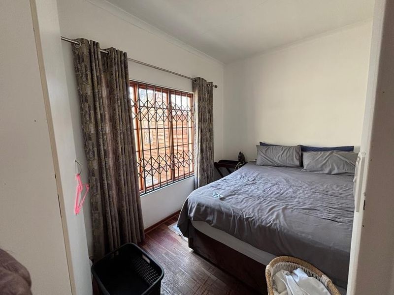 A functional bedroom featuring laminate flooring, a window with a security gate, and neutral wall finishes.