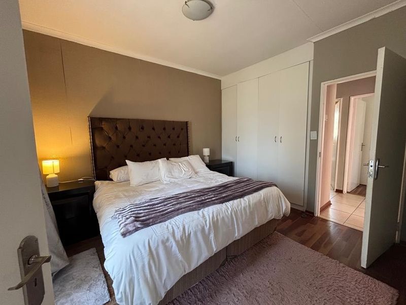A well-proportioned bedroom featuring built-in cupboards, laminate flooring, and direct access to an adjoining hallway.