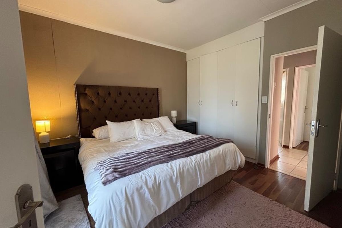 A well-proportioned bedroom featuring built-in cupboards, laminate flooring, and direct access to an adjoining hallway.