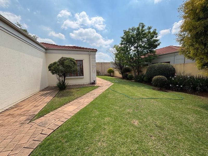 A well-maintained rear garden featuring a paved walkway, manicured lawn, and established boundary walls with mature landscaping.