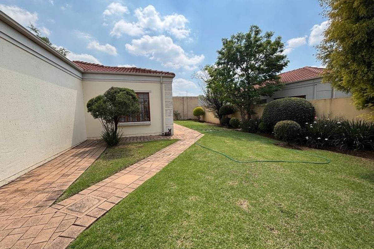 A well-maintained rear garden featuring a paved walkway, manicured lawn, and established boundary walls with mature landscaping.