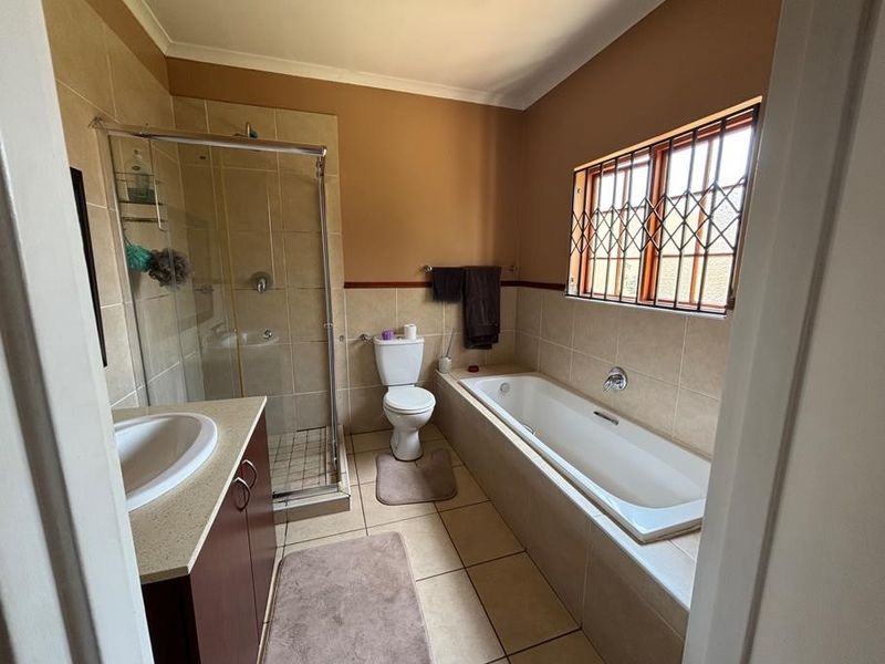 A functional bathroom featuring a separate shower enclosure, a built-in bathtub, a vanity unit, and tiled finishes throughout.