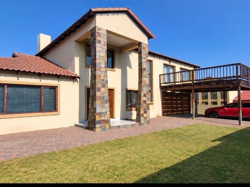 Front elevation of a two-story house featuring stone-clad pillars, a paved driveway, and an elevated wooden balcony.