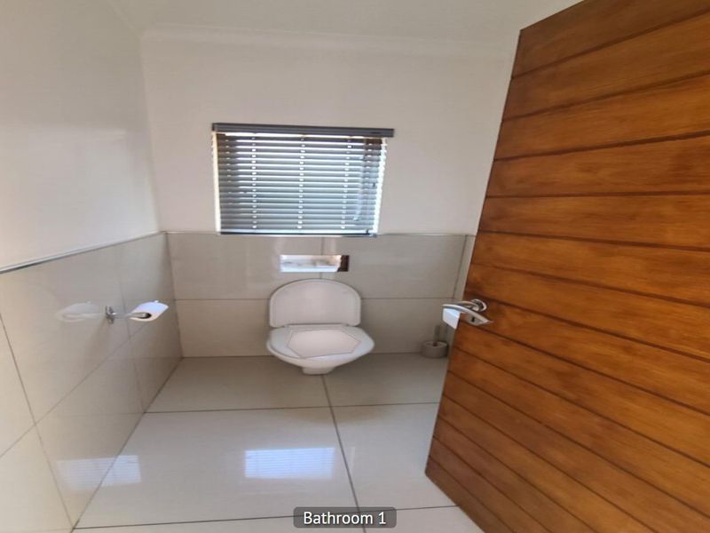 A clean and modern bathroom featuring tiled walls and flooring, a wall-mounted toilet, and a timber door.