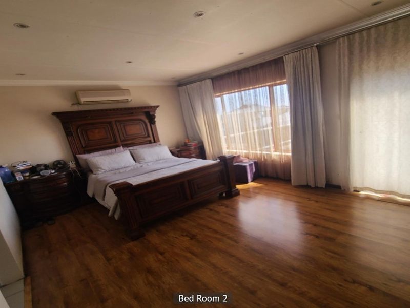 Spacious bedroom featuring warm-toned laminate flooring, recessed ceiling lighting, a wall-mounted air conditioning unit, and large sliding glass doors with curtains.