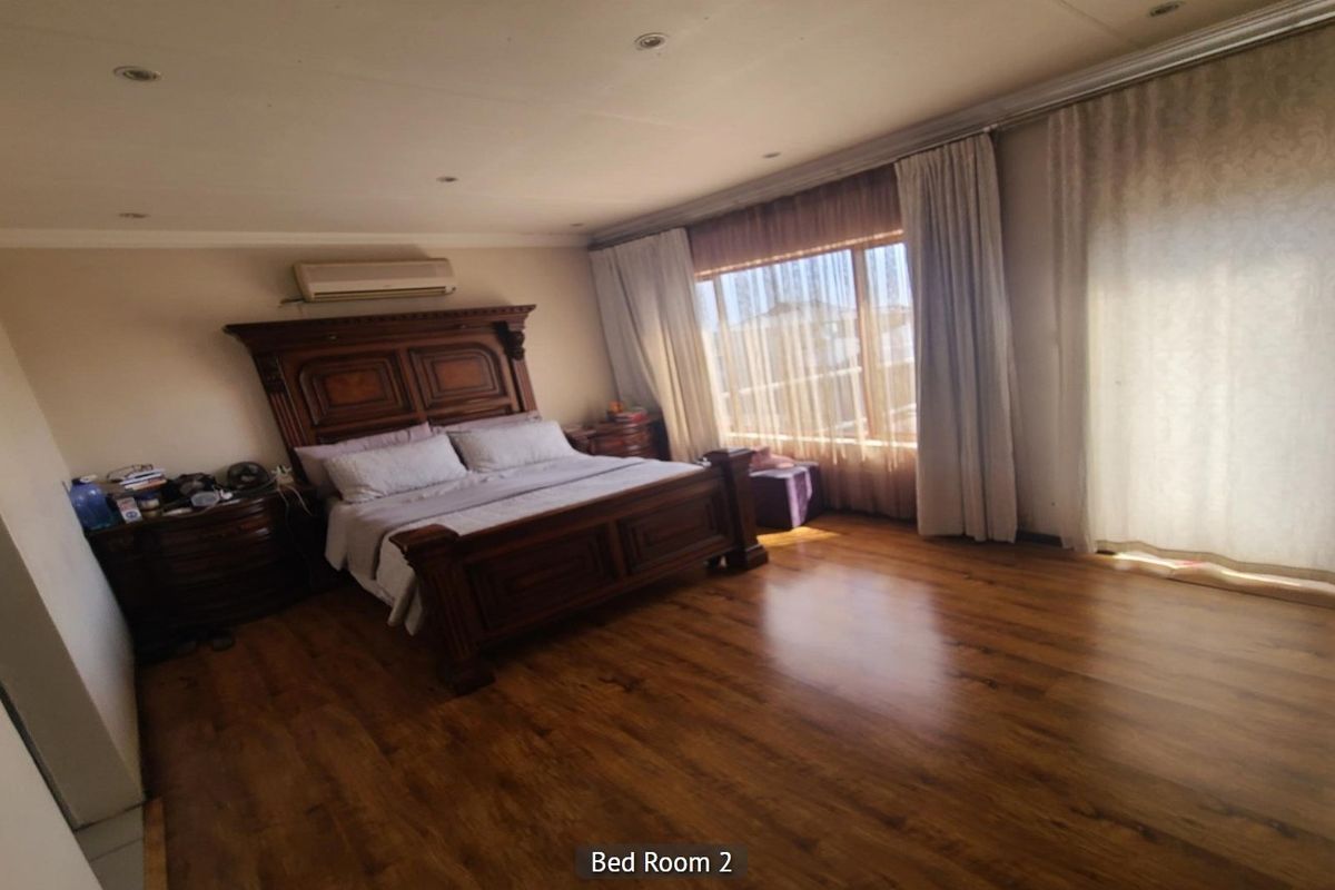 Spacious bedroom featuring warm-toned laminate flooring, recessed ceiling lighting, a wall-mounted air conditioning unit, and large sliding glass doors with curtains.
