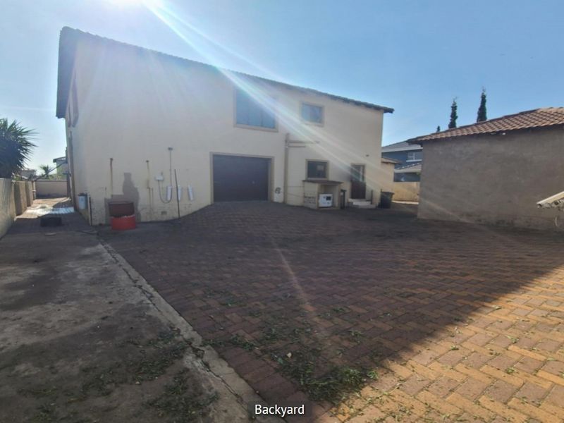 Rear exterior view of the property featuring a paved driveway, garage access, and boundary walling.