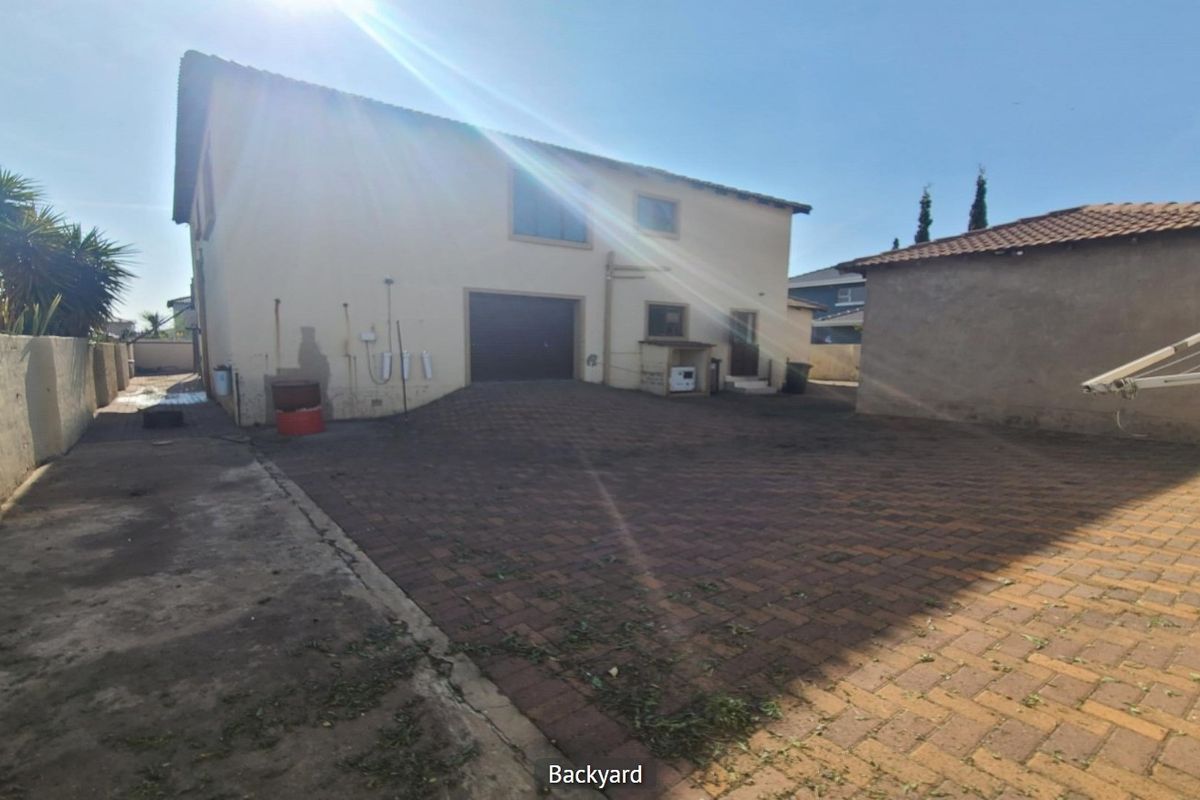 Rear exterior view of the property featuring a paved driveway, garage access, and boundary walling.