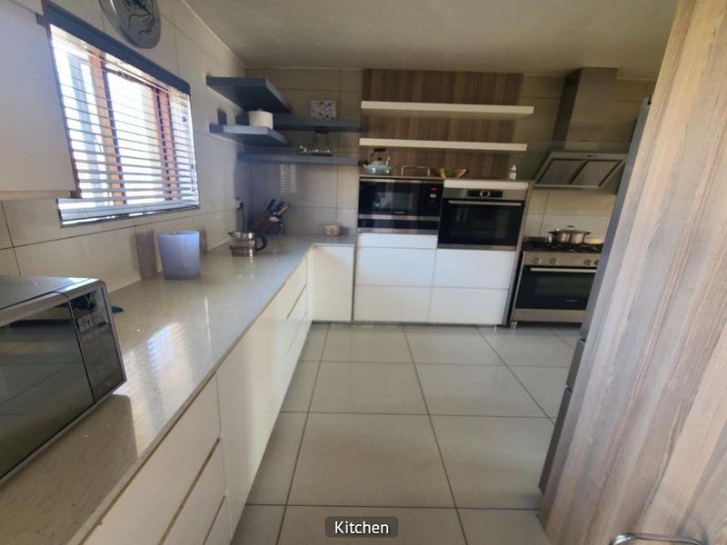 Modern kitchen featuring sleek white cabinetry, stone countertops, built-in oven and microwave, extractor fan, and tiled flooring with floating shelving.