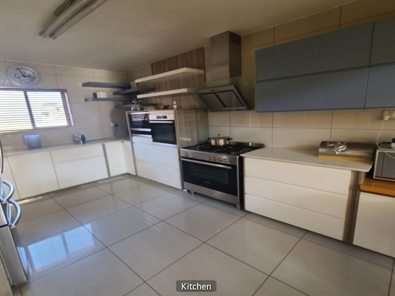 Modern kitchen featuring sleek white and grey cabinetry, stainless steel gas stove with extractor, tiled flooring, and ample counter space.