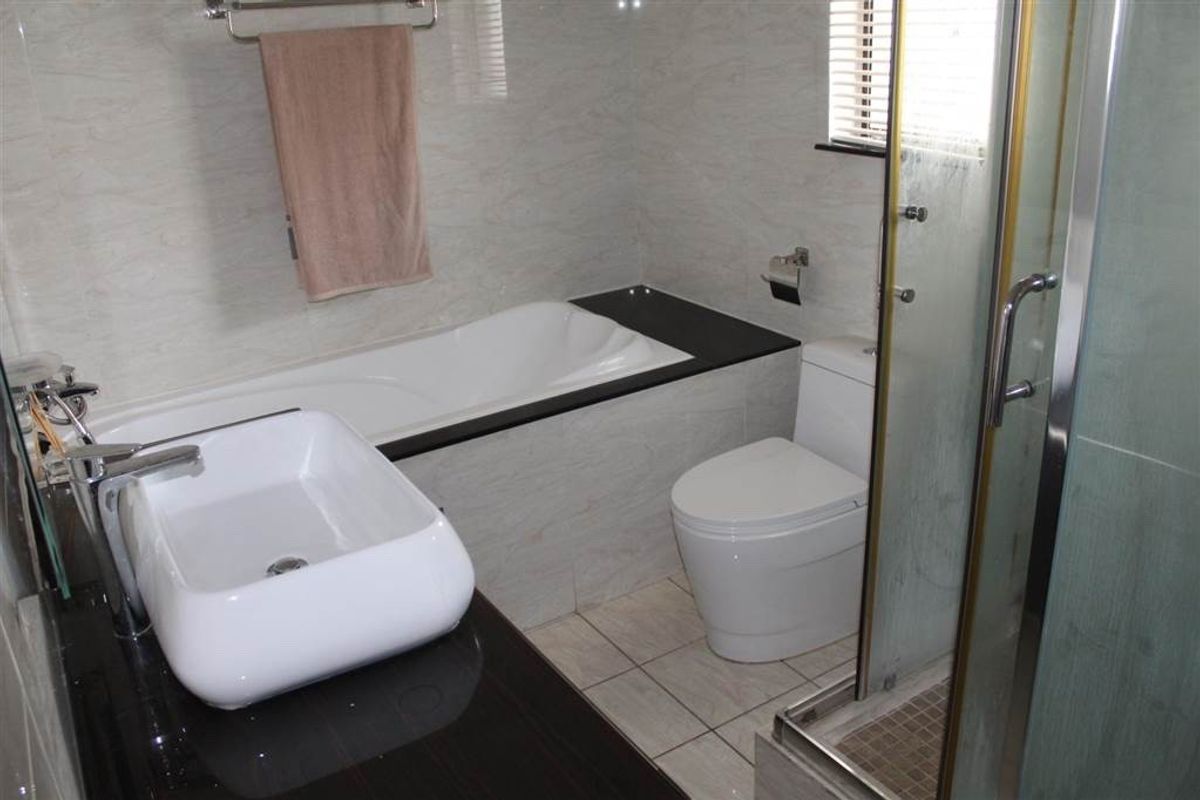 Modern bathroom featuring a built-in bathtub, vessel sink vanity, toilet, and a separate glass-enclosed shower with neutral tiled finishes.