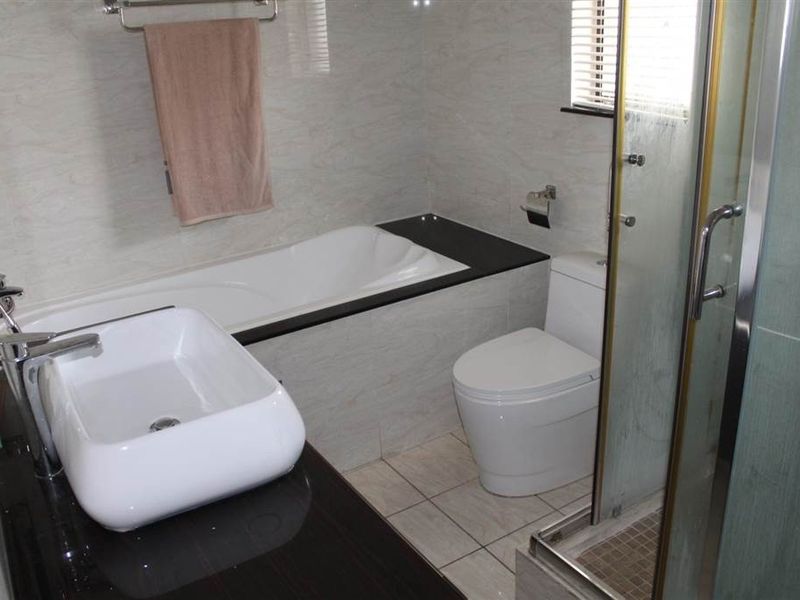 Modern bathroom featuring a built-in bathtub, vessel sink vanity, toilet, and a separate glass-enclosed shower with neutral tiled finishes.