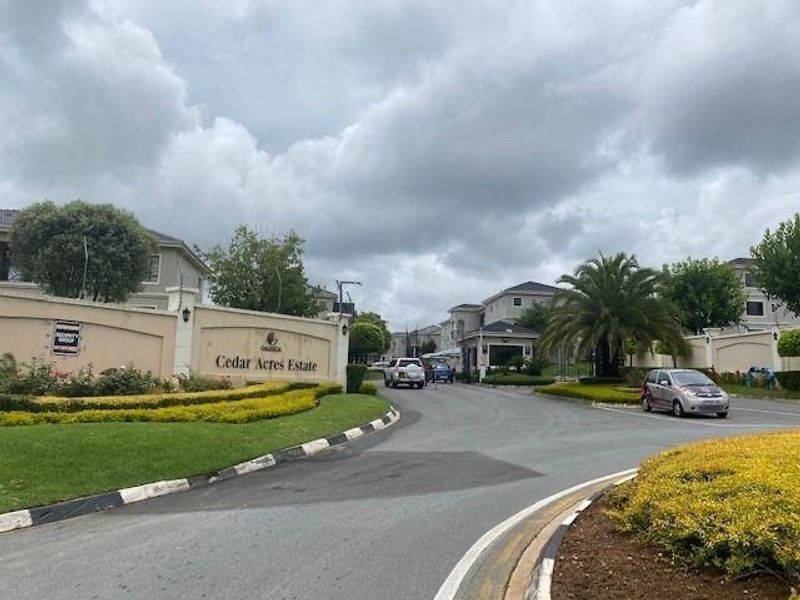 The entrance to Cedar Acres Estate, featuring a gated access point, perimeter walling, and well-maintained landscaped gardens.