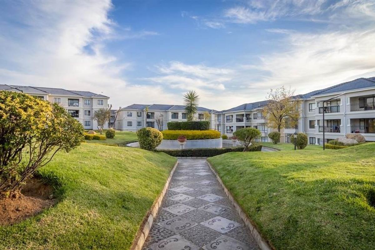 A well-maintained communal garden area featuring a paved walkway and landscaped lawns within an apartment complex setting.