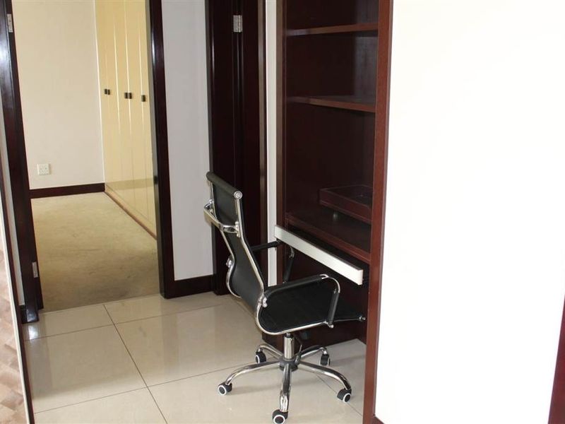 A compact home office area featuring built-in desk space, integrated shelving, and access to a hallway with built-in storage cupboards.