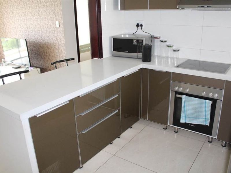 Modern kitchen featuring high-gloss cabinetry, quartz countertops, integrated electric hob, oven, and extractor fan, complemented by neutral tiled flooring and backsplash.