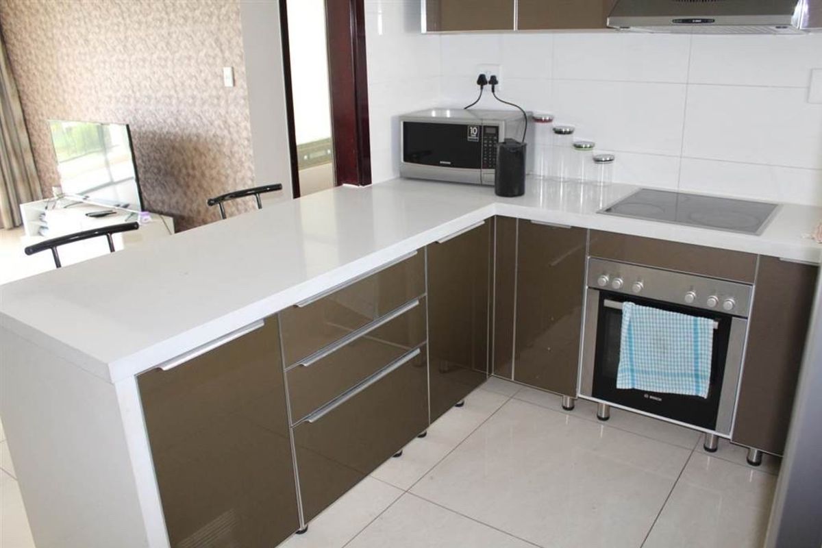 Modern kitchen featuring high-gloss cabinetry, quartz countertops, integrated electric hob, oven, and extractor fan, complemented by neutral tiled flooring and backsplash.