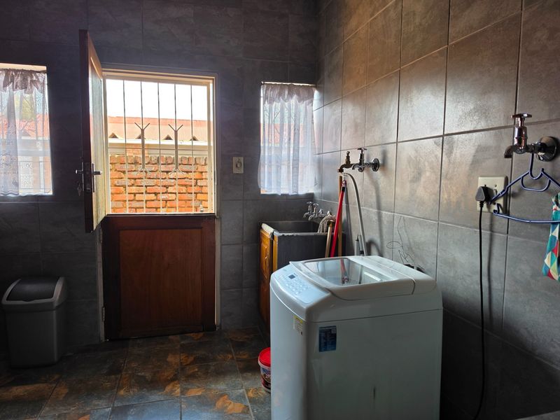 A functional laundry room featuring full-height wall tiling, a utility sink, and dedicated plumbing connections for appliances, with direct access to the exterior.