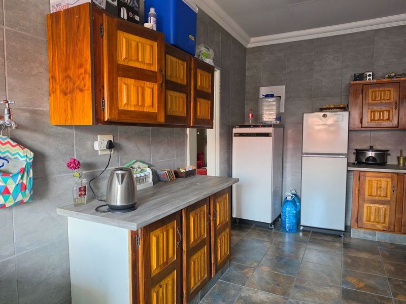 A functional kitchen featuring wooden cabinetry, grey tiled walls, and tiled flooring, providing a practical workspace with ample storage.
