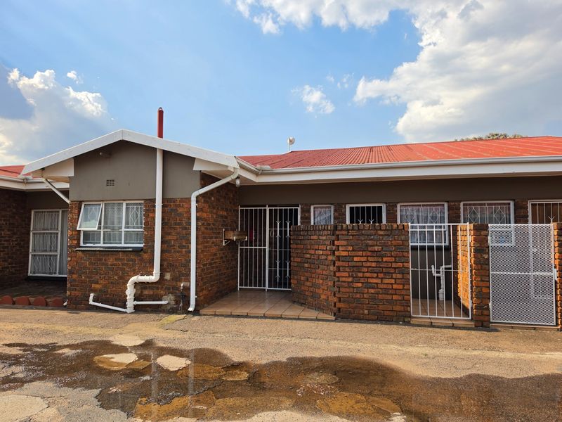 Front exterior view of a face brick apartment unit featuring a corrugated metal roof, security gates, and a tiled entrance area.