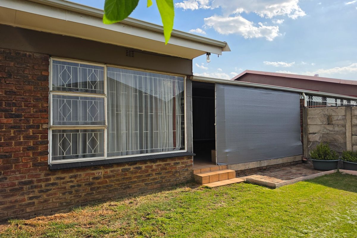 Rear view of the apartment featuring a brick facade, security-barred windows, and a small tiled patio area leading to the garden.