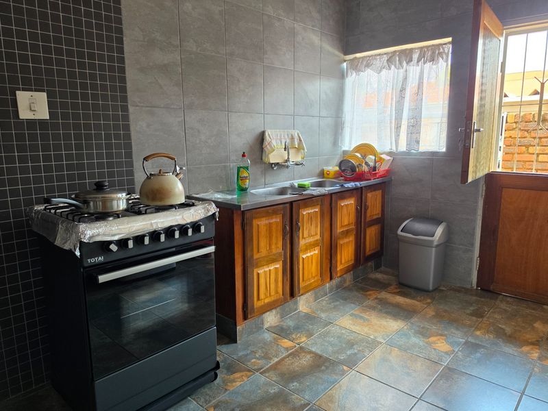 A functional kitchen featuring wooden cabinetry, a stainless steel sink, tiled backsplash, and a gas stove with direct access to an outdoor area.