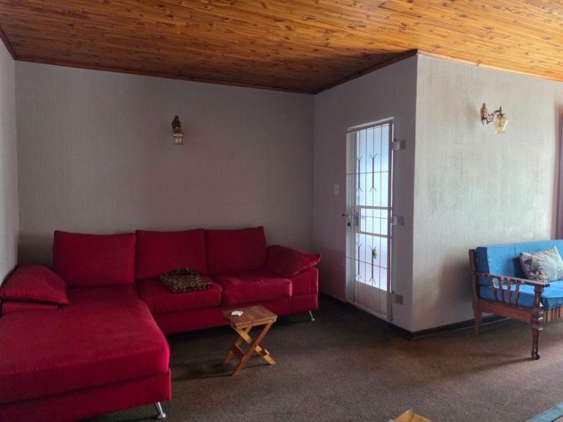 A living room featuring a timber-clad ceiling, wall-mounted lighting fixtures, and a security gate leading to an exterior area.