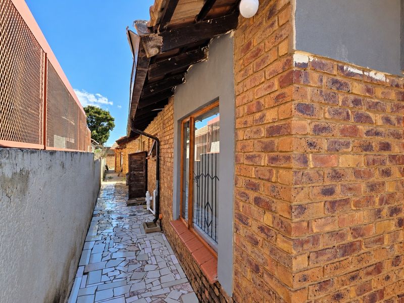 A side exterior view of the property featuring exposed brick walls, tiled pathway, and security-fitted windows along the narrow side passage.