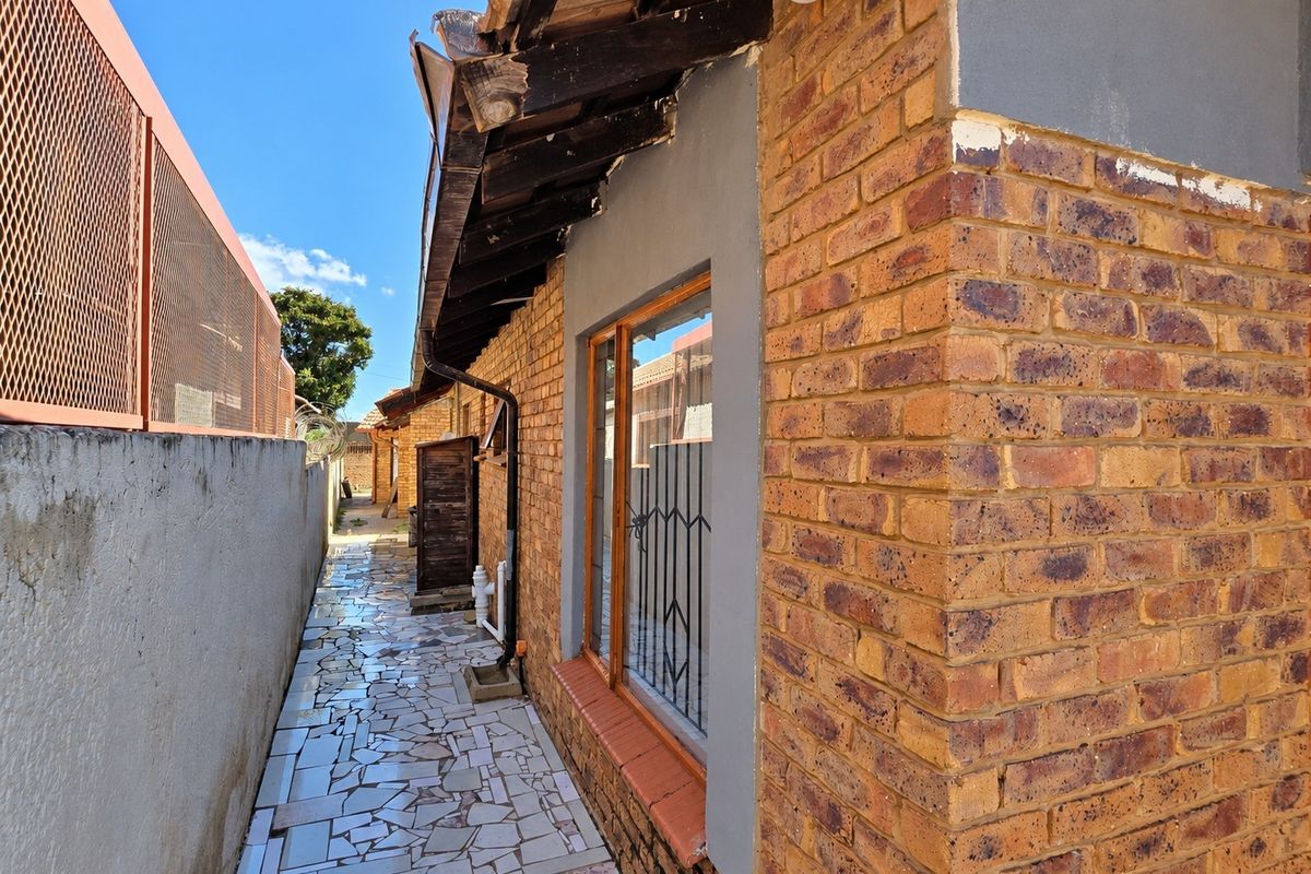 A side exterior view of the property featuring exposed brick walls, tiled pathway, and security-fitted windows along the narrow side passage.