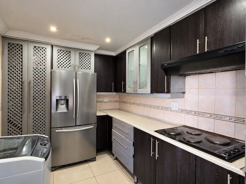 A functional kitchen featuring dark wood cabinetry, light countertops, an electric hob with extractor fan, and tiled finishes, showing minor ceiling water damage.