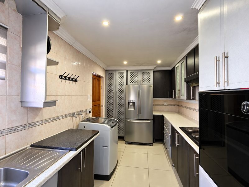 A functional kitchen featuring dark cabinetry, stone countertops, built-in oven, hob, and extractor fan, with tiled backsplash and recessed lighting throughout.