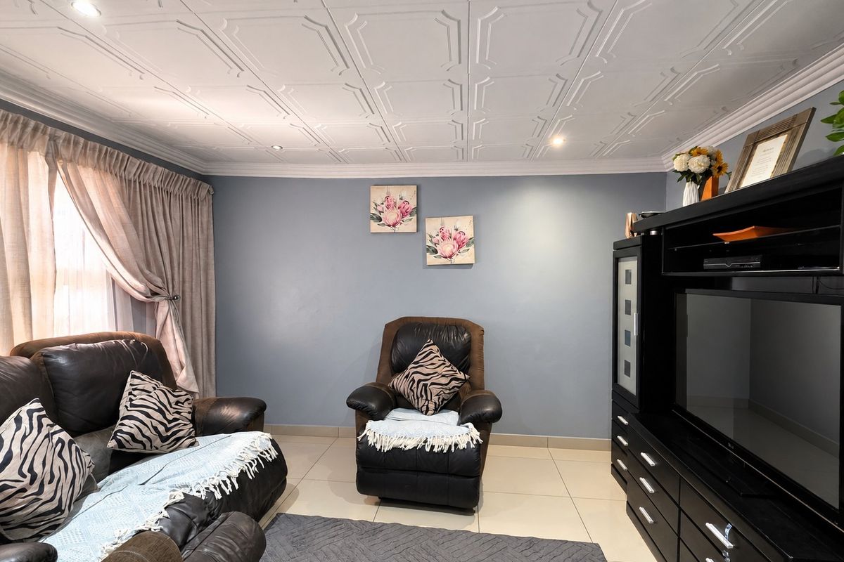 A comfortable living room featuring decorative ceiling tiles, recessed downlighting, and neutral tiled flooring, providing a well-maintained and functional space.