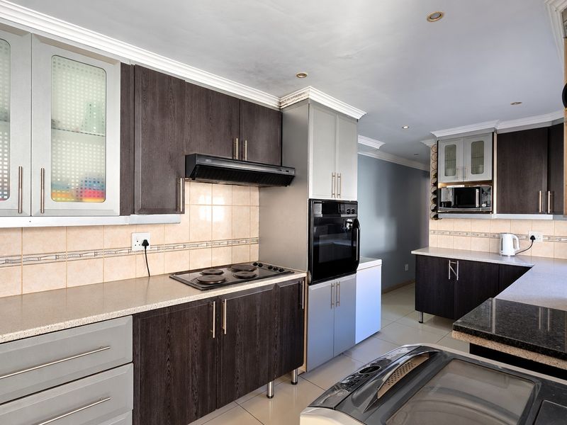 Modern kitchen featuring dark wood-grain cabinetry, built-in oven and hob, tiled backsplash, and ample counter space with recessed lighting.