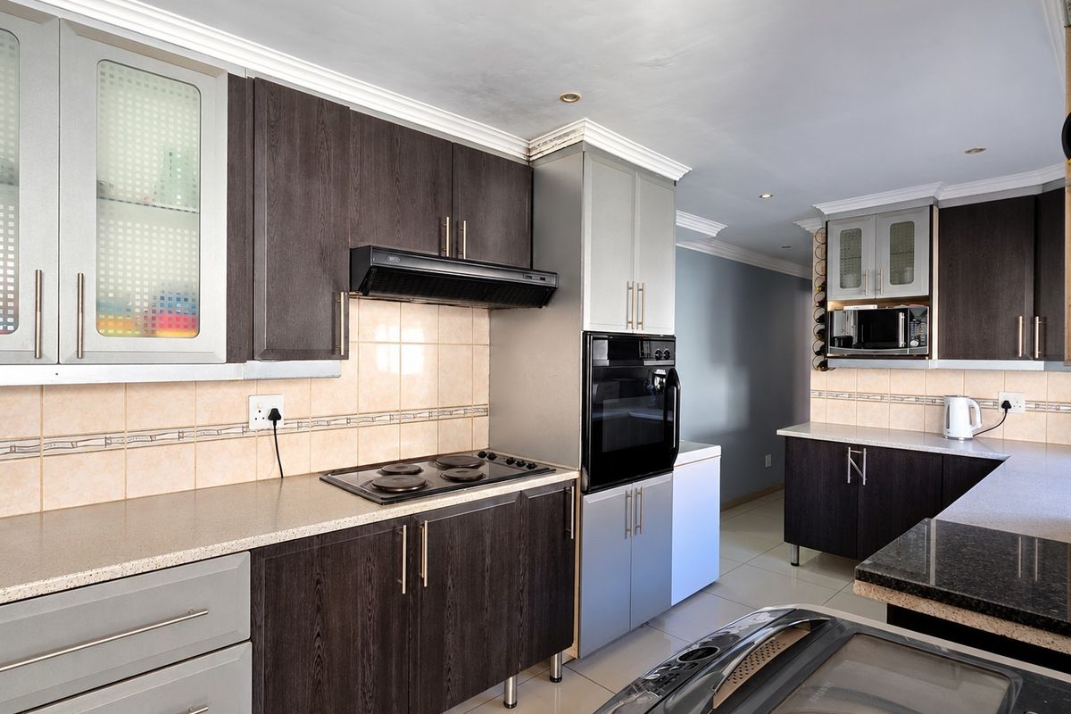 Modern kitchen featuring dark wood-grain cabinetry, built-in oven and hob, tiled backsplash, and ample counter space with recessed lighting.