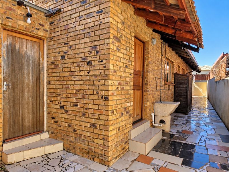 Rear exterior view featuring face brick walls, a tiled patio area, and a functional concrete wash basin under exposed timber rafters.