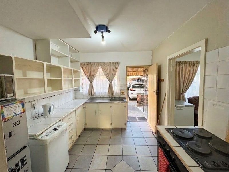 A functional kitchen featuring tiled countertops, built-in cabinetry, and a tiled backsplash, with direct access to the exterior parking area.