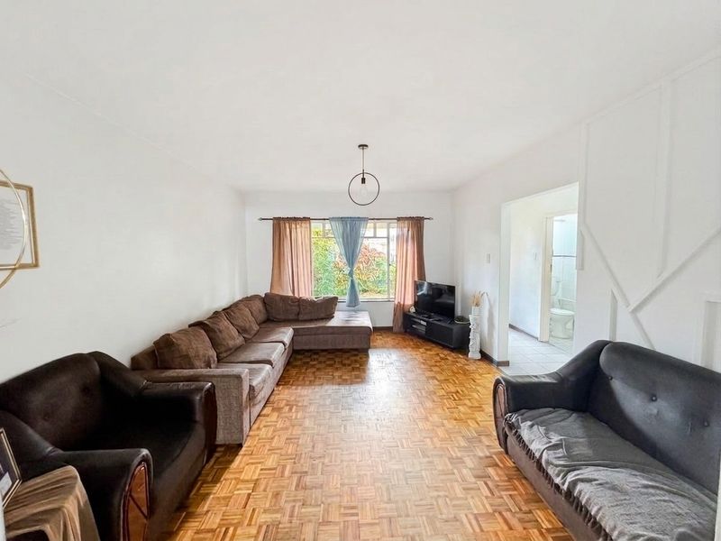 Spacious living room featuring classic parquet flooring and natural light, with an adjacent hallway leading to a bathroom.