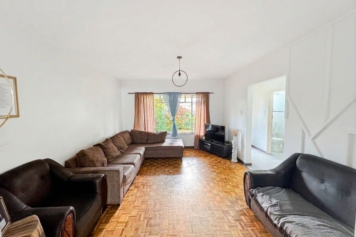 Spacious living room featuring classic parquet flooring and natural light, with an adjacent hallway leading to a bathroom.