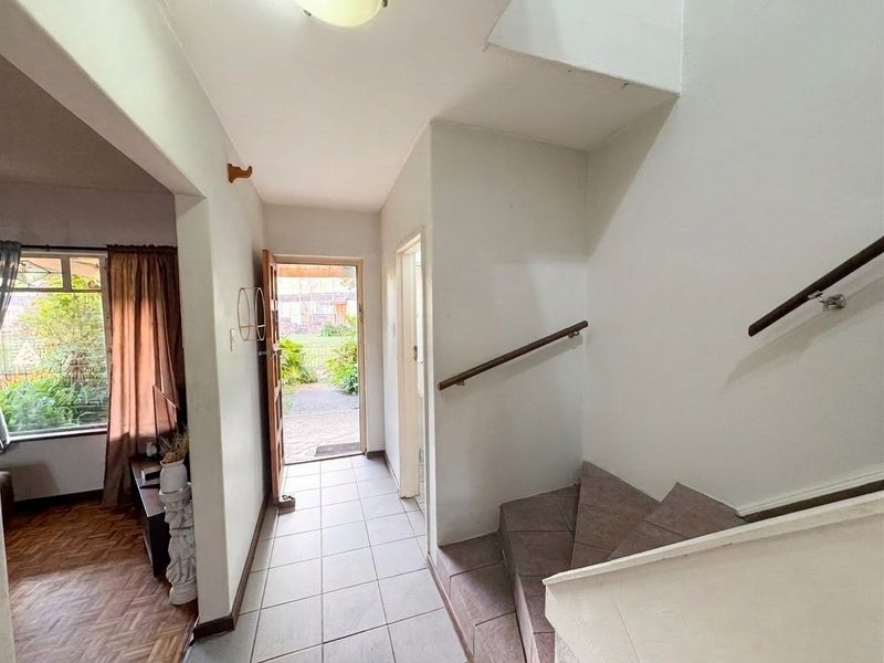 Entrance hallway featuring tiled flooring and a staircase with a wooden handrail, providing direct access to the living area and front exterior.