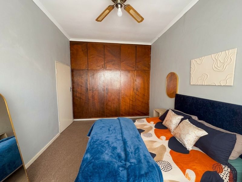 A bedroom featuring built-in wooden cupboards, a ceiling fan, and carpeted flooring, offering a functional space with potential for modern updates.
