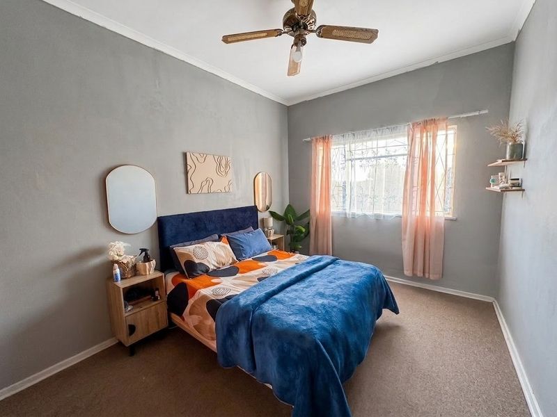 A cozy bedroom featuring carpeted flooring, a ceiling fan, and security bars on the window, providing a functional and comfortable living space.