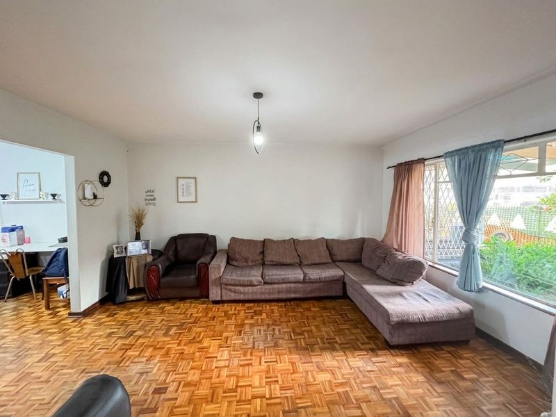 Spacious living room featuring classic parquet flooring, a large window with security bars, and a central pendant light fixture.