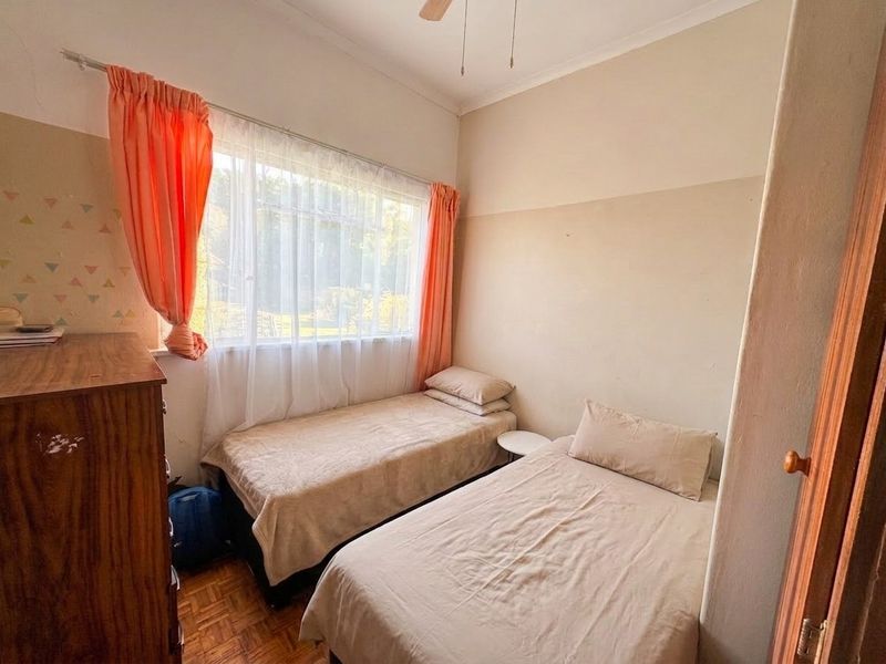 A bedroom featuring parquet flooring, a ceiling fan, and a large window, currently showing signs of wear on the walls.